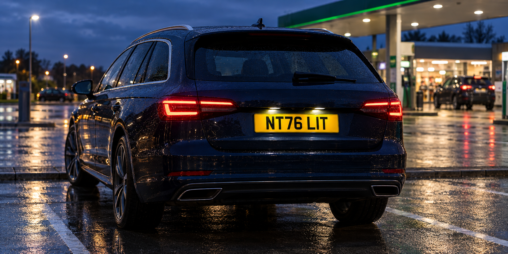 Rear of a dark blue estate car at rainy twilight with its complete yellow NT76 LIT plate illuminated